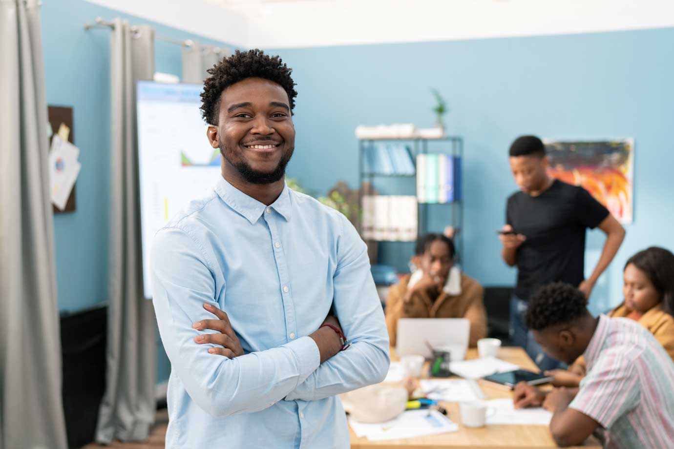 Young man smiling in a room full of colleagues working on a project